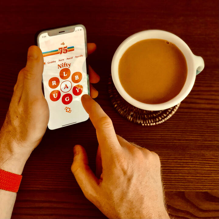 Person playing Retrogram on iPhone next to a cup of coffee