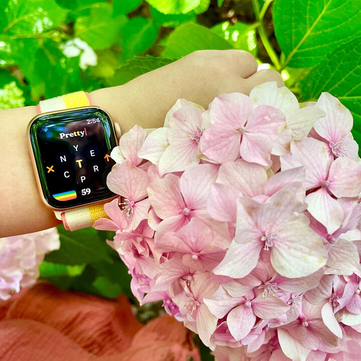 Apple Watch worn on wrist near flowers, watch displays Retrogram game screen